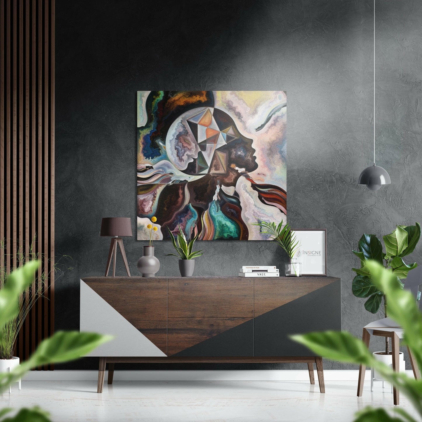 Modern interior with colorful abstract portrait artwork hung above wooden dresser with plants and pendant lamp.