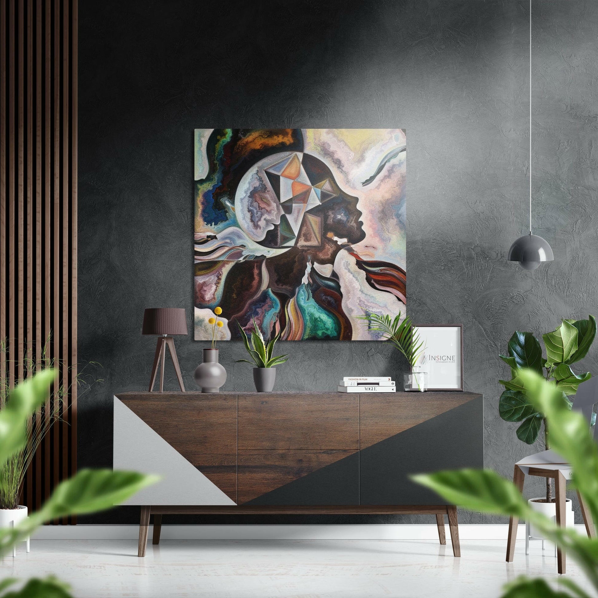 Modern interior with colorful abstract portrait artwork hung above wooden dresser with plants and pendant lamp.