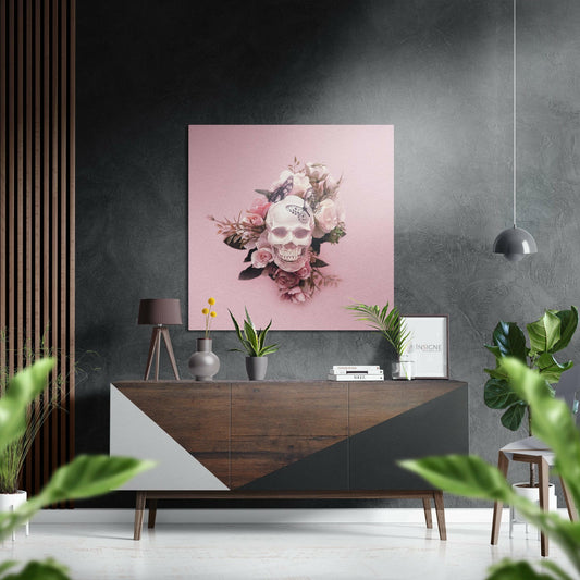 Modern interior display featuring blush pink square artwork with skull and floral design mounted on textured gray wall above wooden dresser.