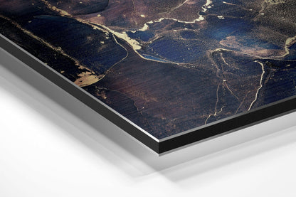 Angled close-up of brushed aluminium Dibond wall art showing aerial landscape with winding rivers, dark forests, and golden light reflections.