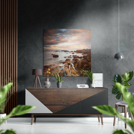 Coast Brushed Aluminium Dibond Wall Art depicting rocky shoreline at sunset, displayed above wooden sideboard in modern interior.