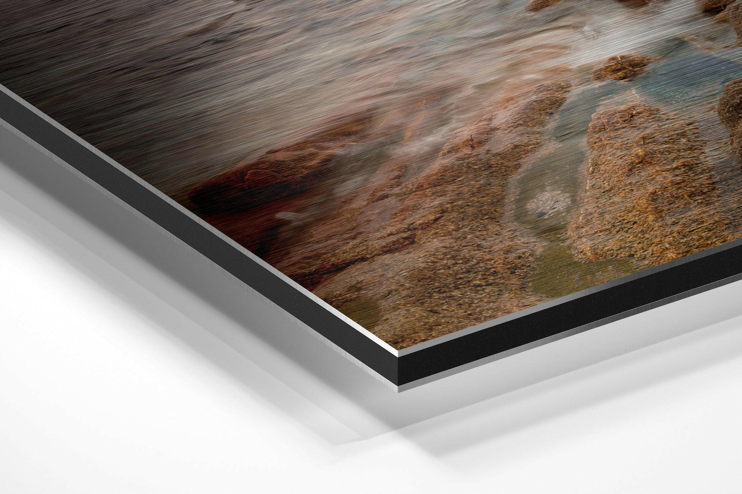 Close-up angled view of brushed aluminium and black edge framing showing coastal rocks and flowing water photograph on Dibond mount.