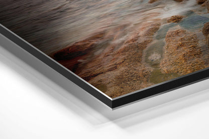 Close-up angled view of brushed aluminium and black edge framing showing coastal rocks and flowing water photograph on Dibond mount.