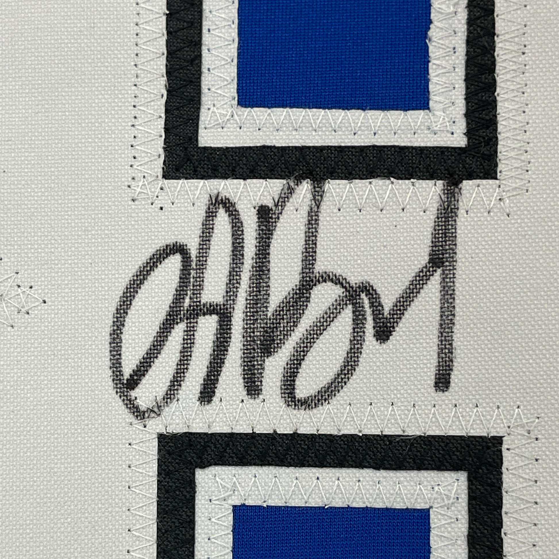 Close-up of embroidered signature "Vasilevskiy" on white fabric between black and blue sections of jersey with zigzag stitching.