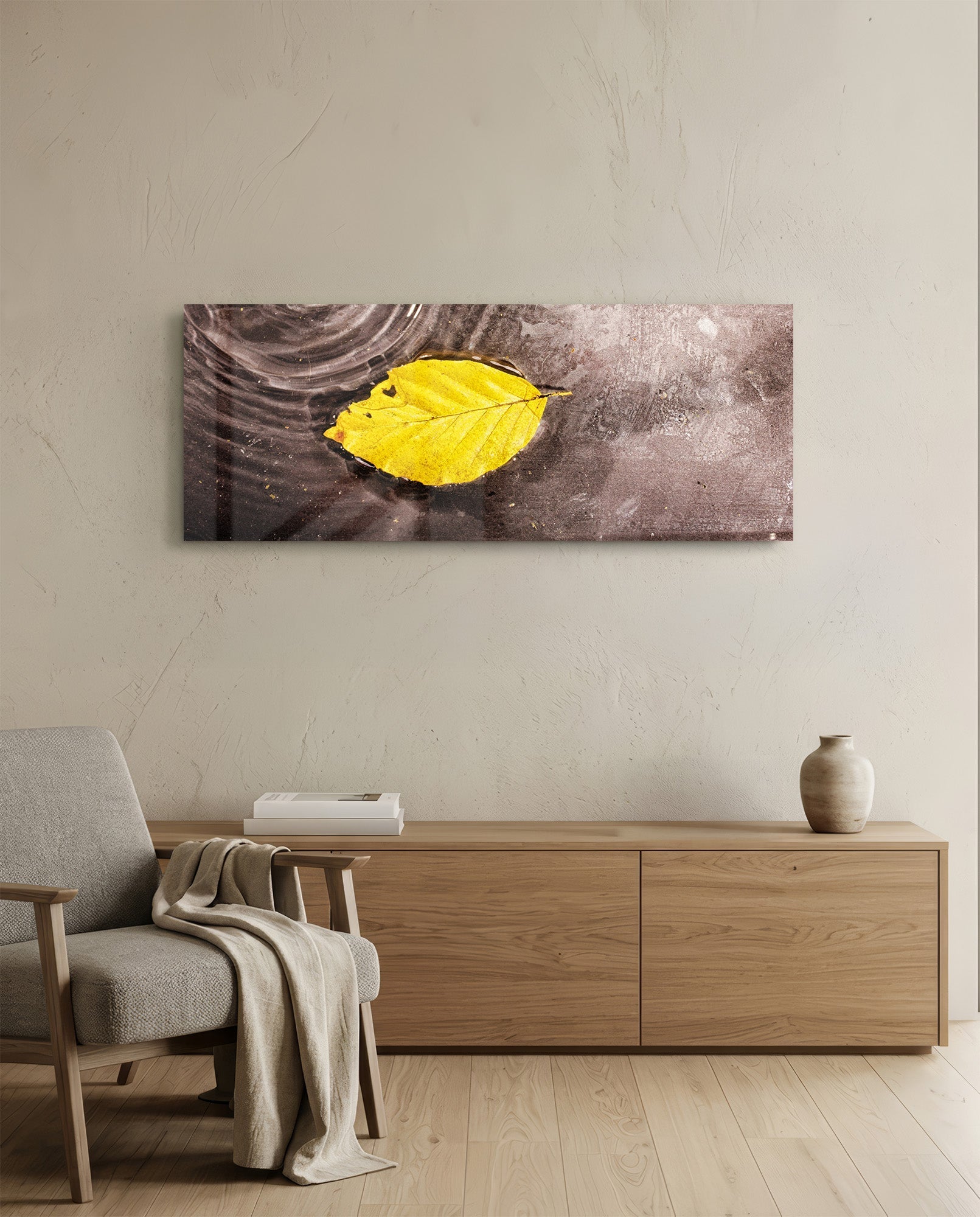 Yellow leaf glass wall art hanging above wooden dresser in minimalist room with beige chair and cream wall.
