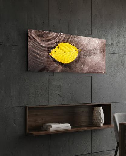 Horizontal glass wall art displaying a bright yellow autumn leaf on a dark weathered wood background, hung above a wooden shelf.