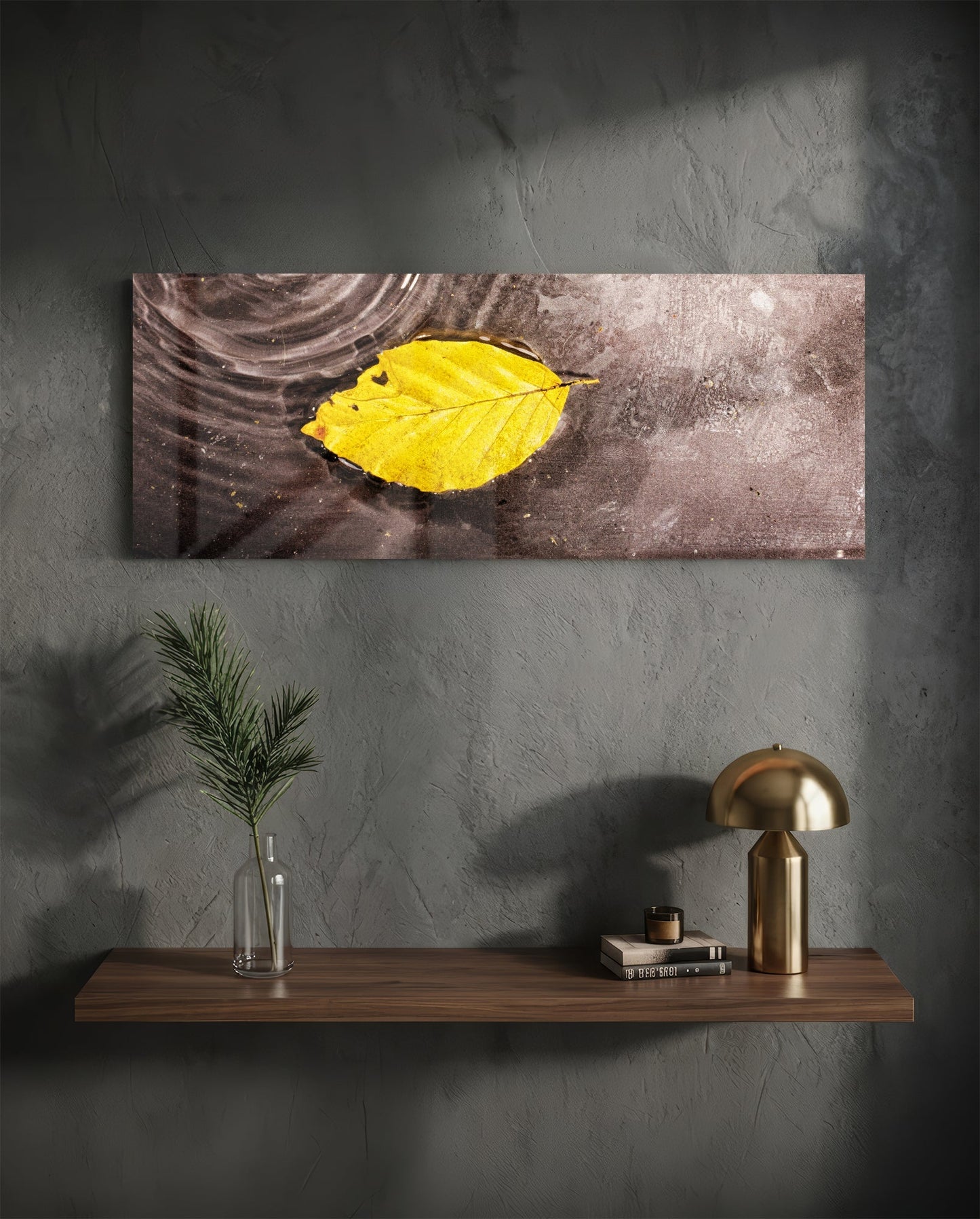 Yellow leaf glass wall art displayed above a wooden shelf with brass lamp and potted plant against textured gray wall.