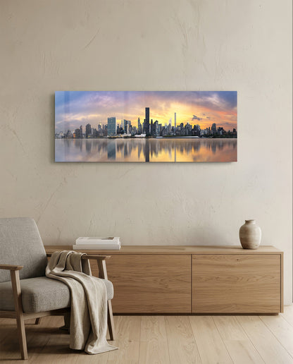 Manhattan skyline at sunset reflected in still water, displayed as a horizontal glass panel above a wooden dresser in a minimalist room.