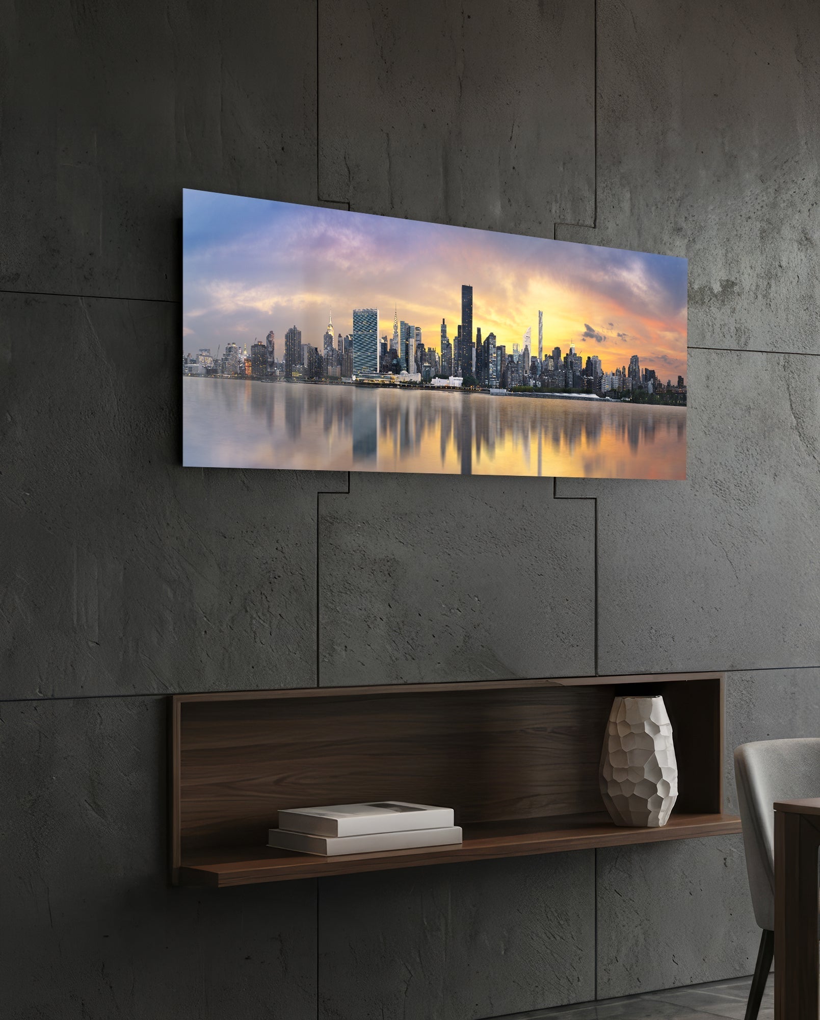NYC skyline glass wall art mounted on concrete wall above wooden shelf, showing sunset reflection on water.