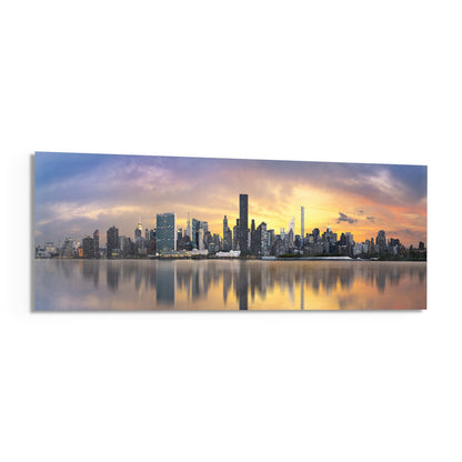 Manhattan skyline at sunset reflected in calm water, printed on horizontal glass panel with warm orange and blue tones.