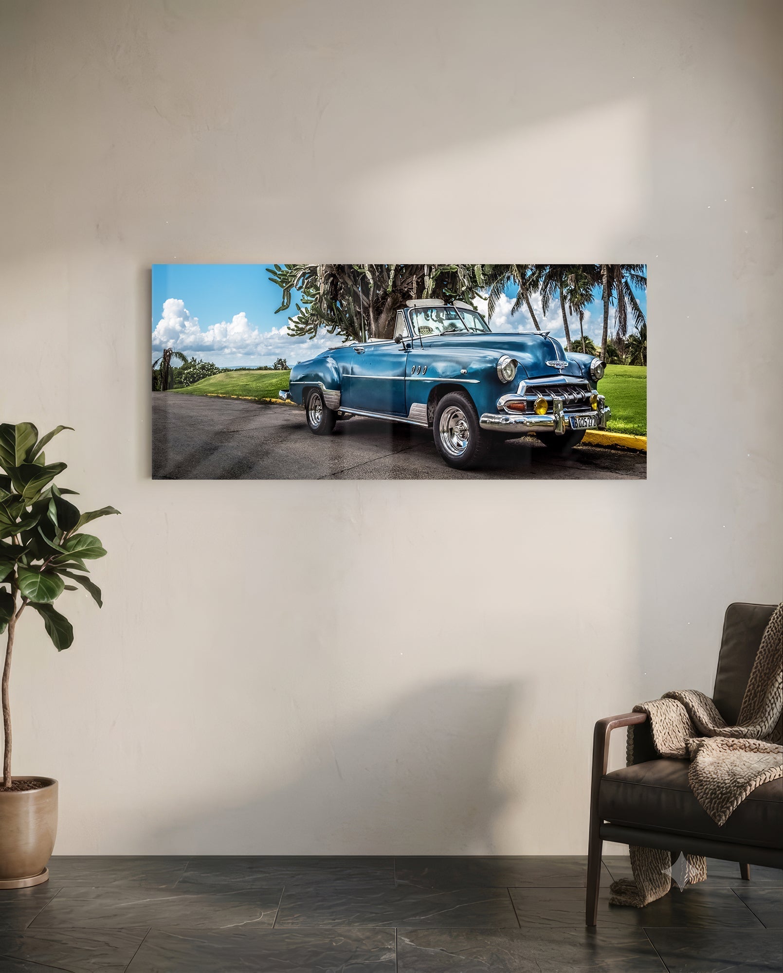 Blue vintage convertible parked under palm trees with green grass and cloudy sky in background.