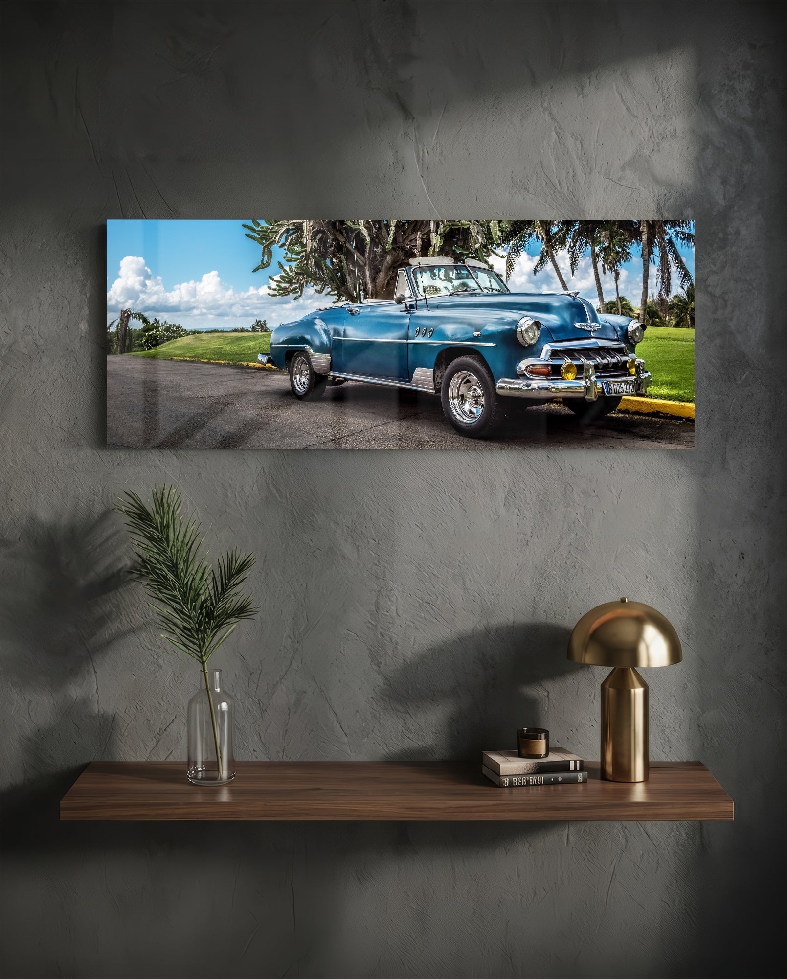 Blue vintage convertible car parked under palm trees with yellow bumper and white-wall tires displayed on gray wall above wooden shelf.