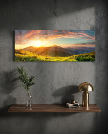 Landscape glass wall art displaying a golden sunset over mountains and grass fields, mounted above a wooden shelf with brass lamp and accessories.