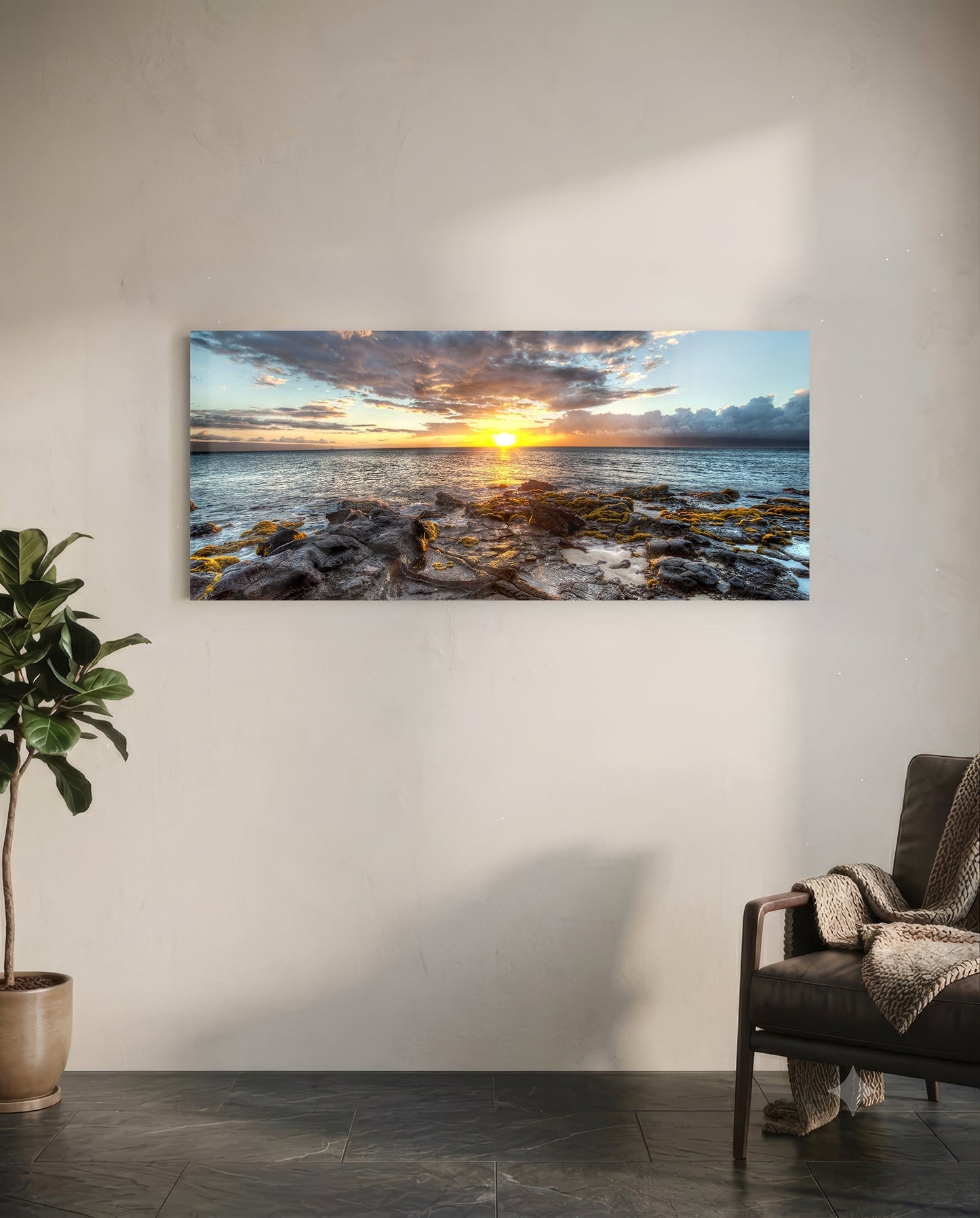 Horizontal glass wall art displaying a coastal sunset with rocky shoreline, golden sun, and dramatic cloudy sky mounted above a leather chair in a modern interior.
