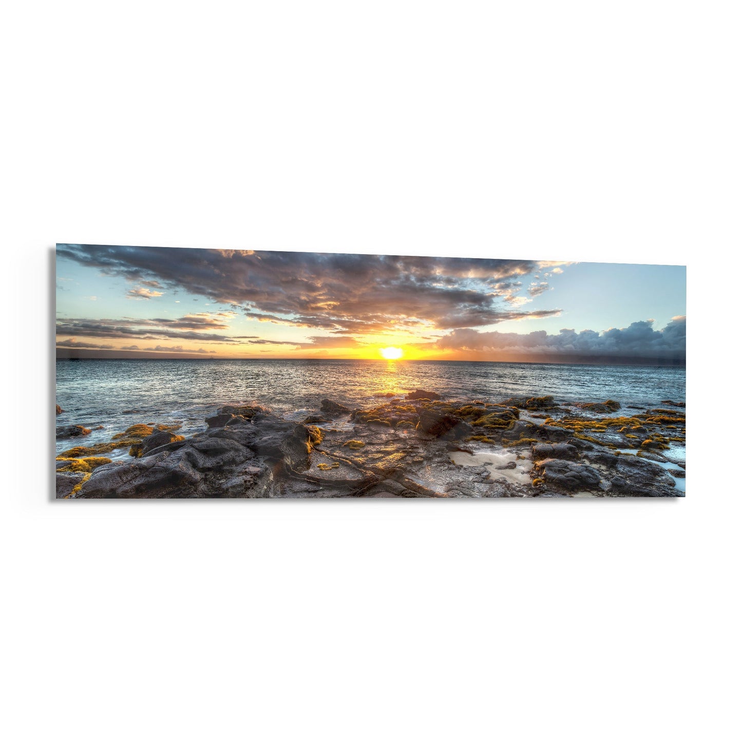 Panoramic glass wall art depicting a golden sunset over rocky coastline with calm ocean waters and dramatic cloudy sky.