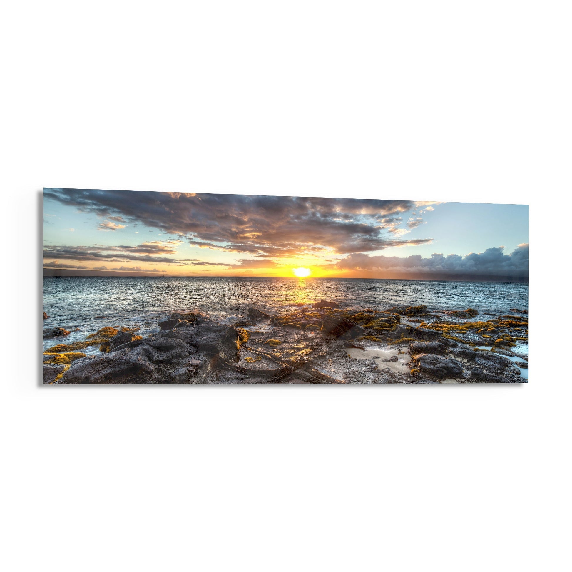 Panoramic glass wall art depicting a golden sunset over rocky coastline with calm ocean waters and dramatic cloudy sky.