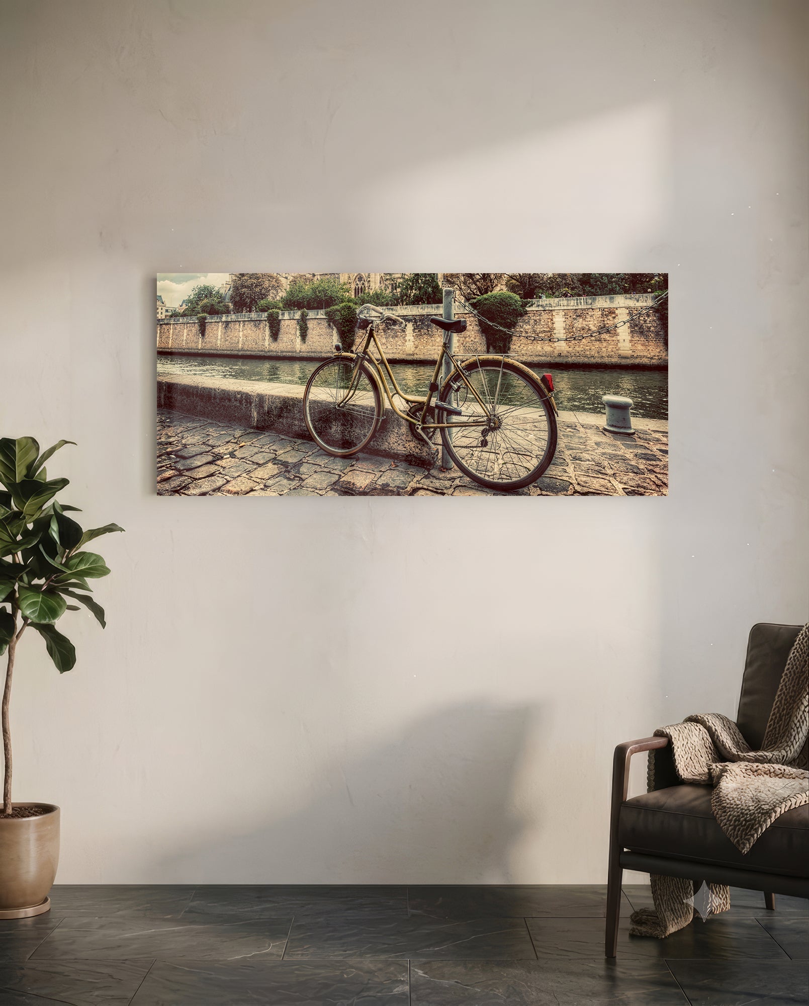 Vintage bicycle leaned against stone wall beside canal with sepia-toned finish displayed on white wall above leather chair.