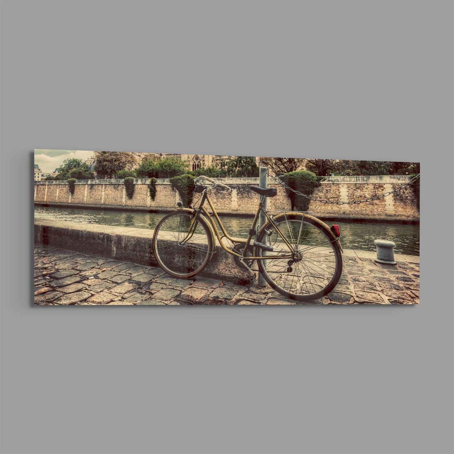 Vintage bicycle leaned against stone riverside wall with Gothic cathedral visible across the water in warm sepia tones.