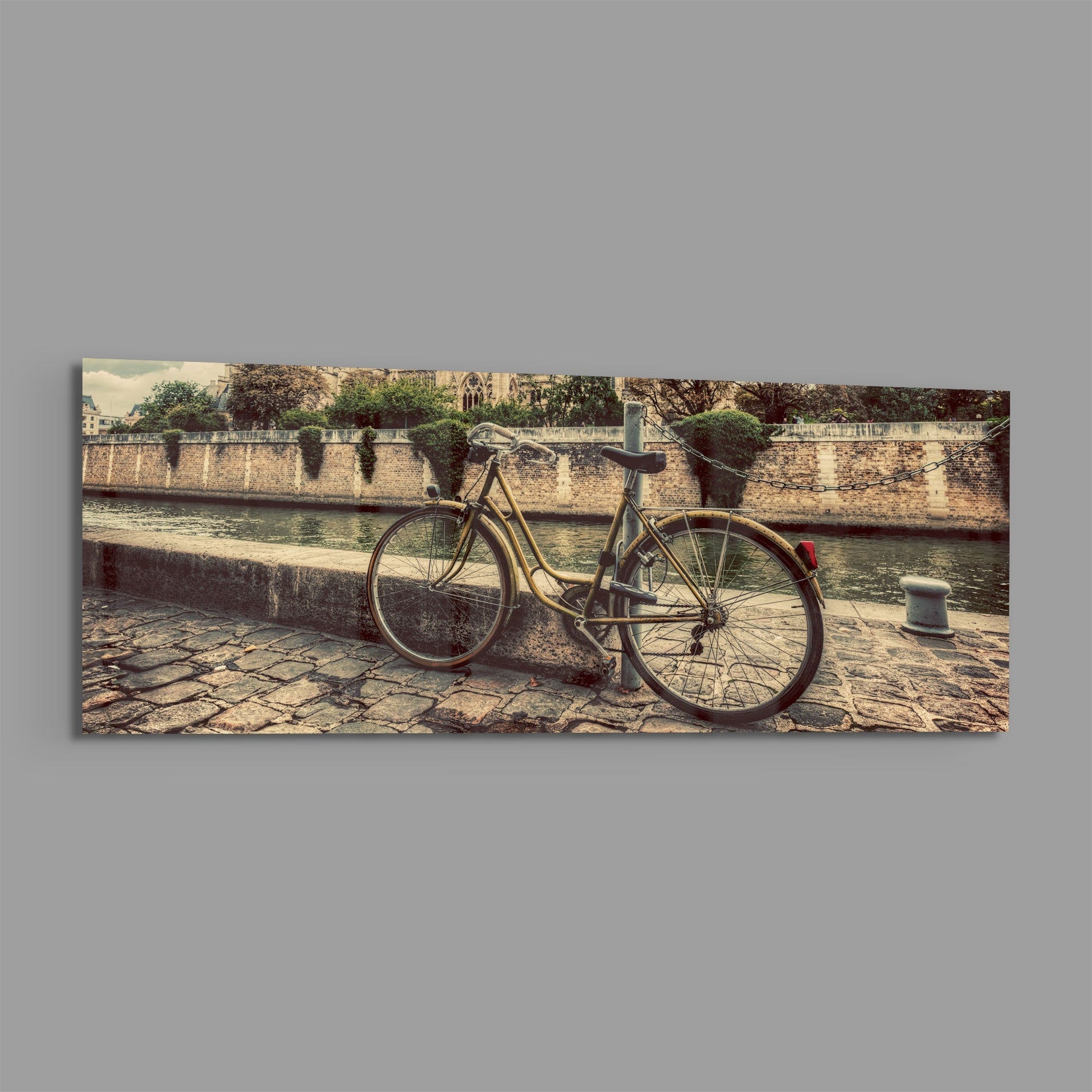 Vintage bicycle leaned against stone riverside wall with Gothic cathedral visible across the water in warm sepia tones.