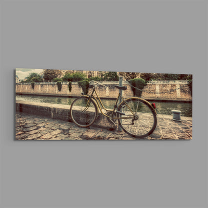 Vintage bicycle leaned against stone riverside wall with Gothic cathedral visible across the water in warm sepia tones.
