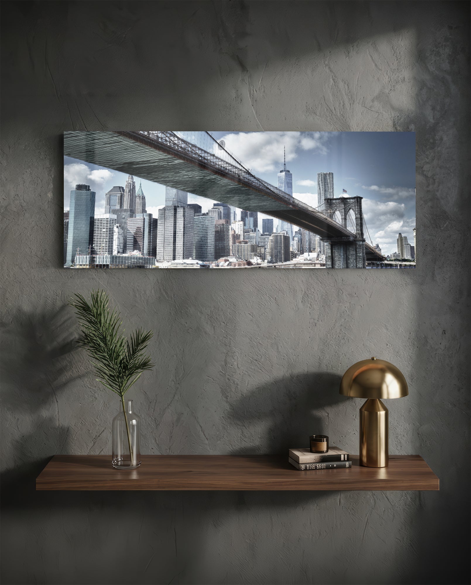 Brooklyn Bridge glass wall art displaying Manhattan skyline and bridge spanning across mounted above wooden shelf with brass lamp and plant vase.