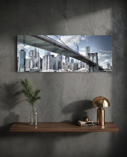 Brooklyn Bridge glass wall art displaying Manhattan skyline and bridge spanning across mounted above wooden shelf with brass lamp and plant vase.