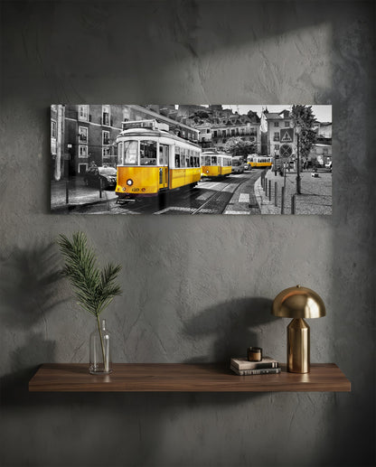 Yellow and black tram on cobblestone street with European buildings, displayed as horizontal glass wall art above wooden shelf.