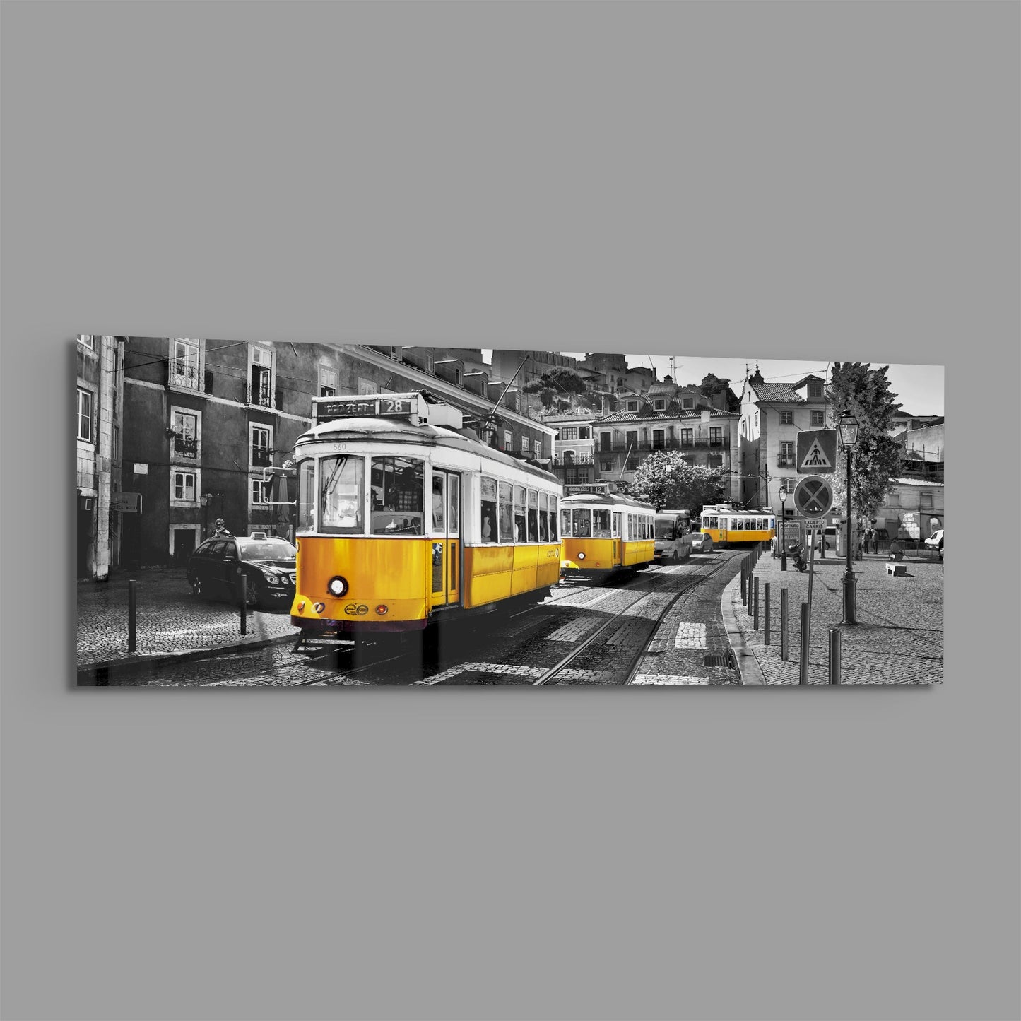 Yellow vintage trams on cobblestone street with selective color photography showing black and white buildings in Lisbon.