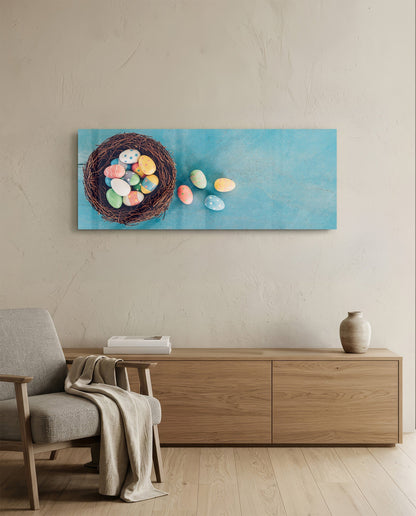 Horizontal glass wall art depicting a woven nest filled with colorful painted eggs on turquoise background, displayed above wooden furniture in modern interior.