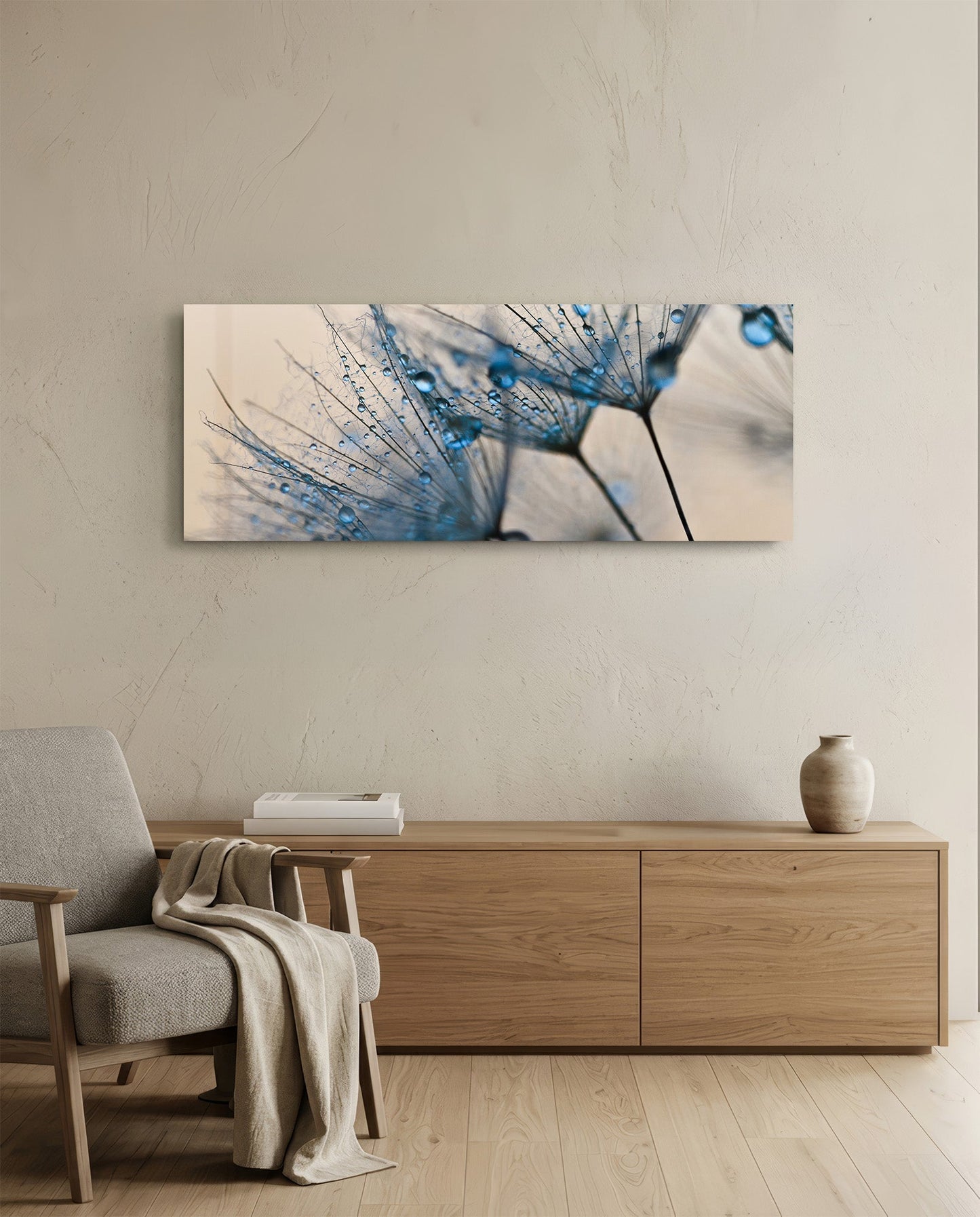 Horizontal glass wall art displaying blue-tinted dandelion seeds with water droplets, hung above wooden furniture in a minimalist interior.