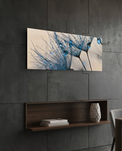 Macro Dandelion Glass Wall Art mounted on dark concrete wall above wooden shelf, displaying blue water droplets on delicate seedhead against cream background.