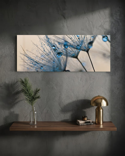 Horizontal glass wall art featuring close-up dandelion seeds with blue water droplets displayed above wooden shelf in modern interior setting.