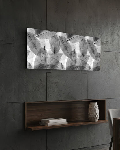 Black and white leaf-patterned glass art displayed horizontally above a wooden shelf on a concrete wall.