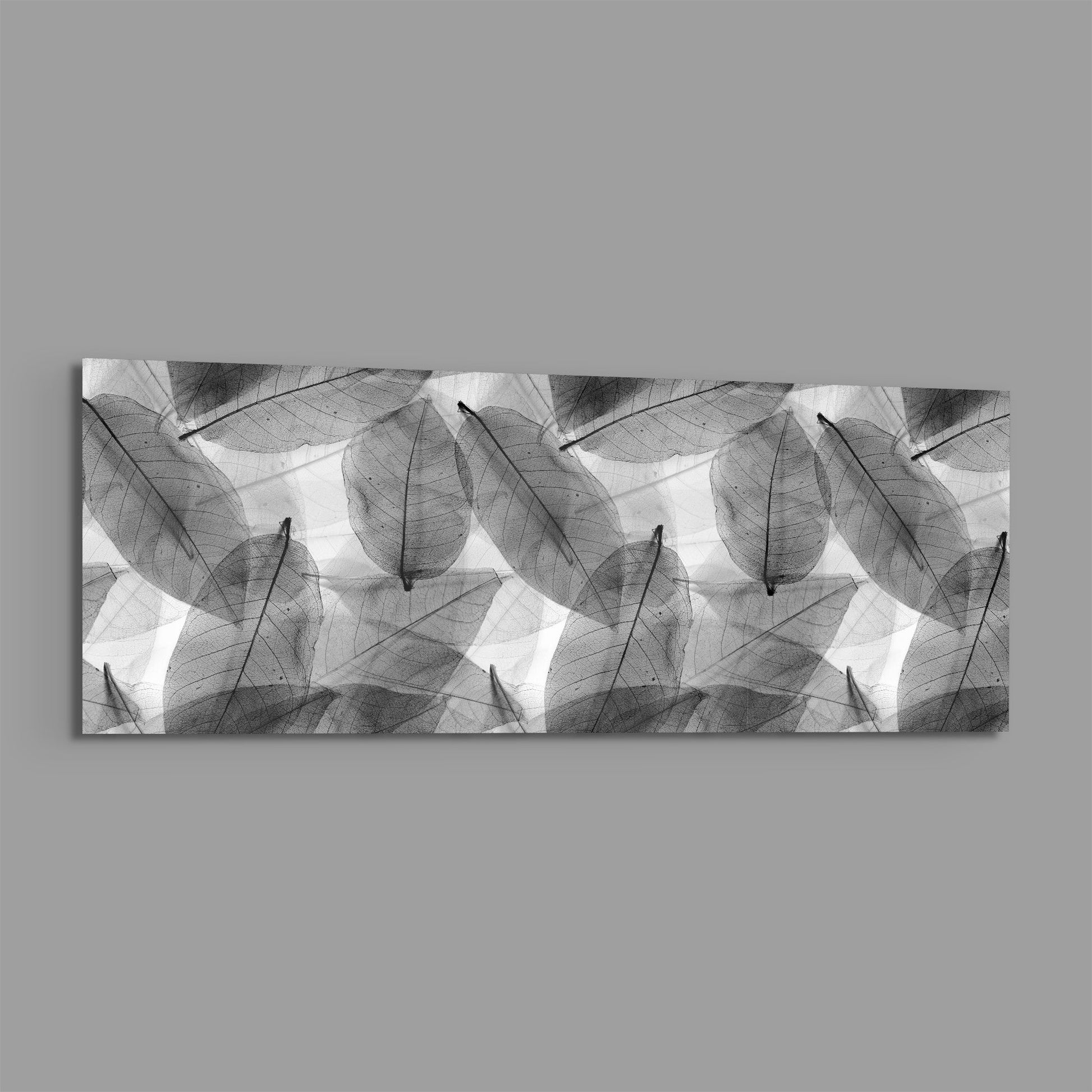 Black and white translucent leaves in overlapping pattern displayed on horizontal rectangular glass wall art against gray background.