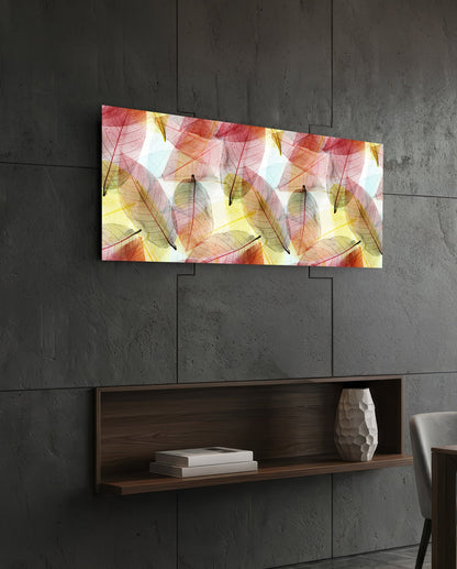 Rectangular glass wall art with translucent red, yellow, and green leaves displayed above a wooden shelf on concrete wall.
