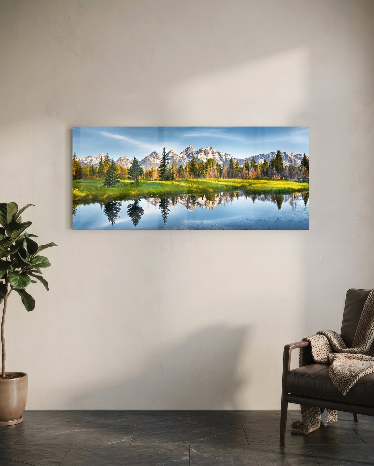 Horizontal glass wall art displaying snow-capped mountains, evergreen forest, and calm reflective water in a modern living room setting.