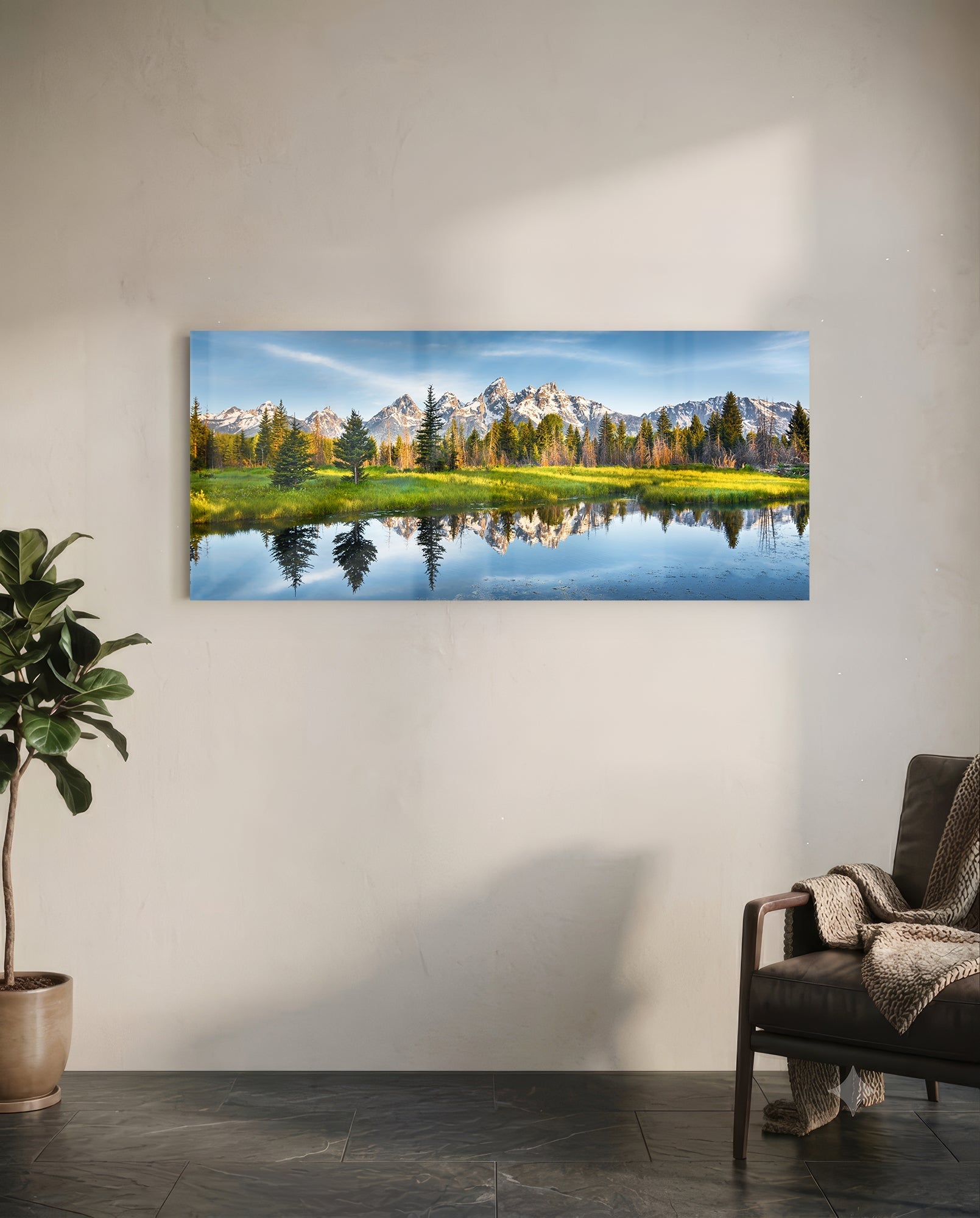 Horizontal glass wall art displaying snow-capped mountains, evergreen forest, and calm reflective water in a modern living room setting.
