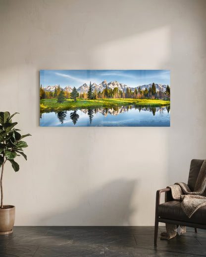 Horizontal glass wall art displaying snow-capped mountains, evergreen forest, and calm reflective water in a modern living room setting.
