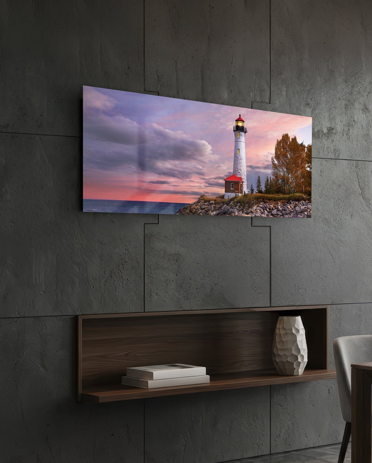 Lighthouse glass wall art mounted on concrete wall above wooden shelf, showing sunset scene with white tower and red keeper's house.
