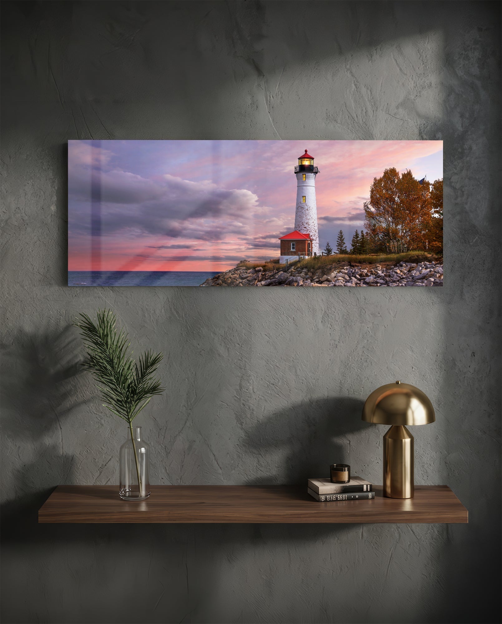 Glass wall art print displaying a white lighthouse with red keeper's house at sunset, mounted above a wooden shelf.