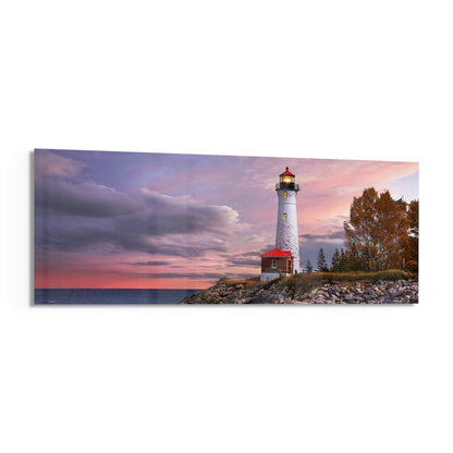 White lighthouse with red keeper's house on rocky shore at sunset, purple and pink sky, evergreen trees, calm water.