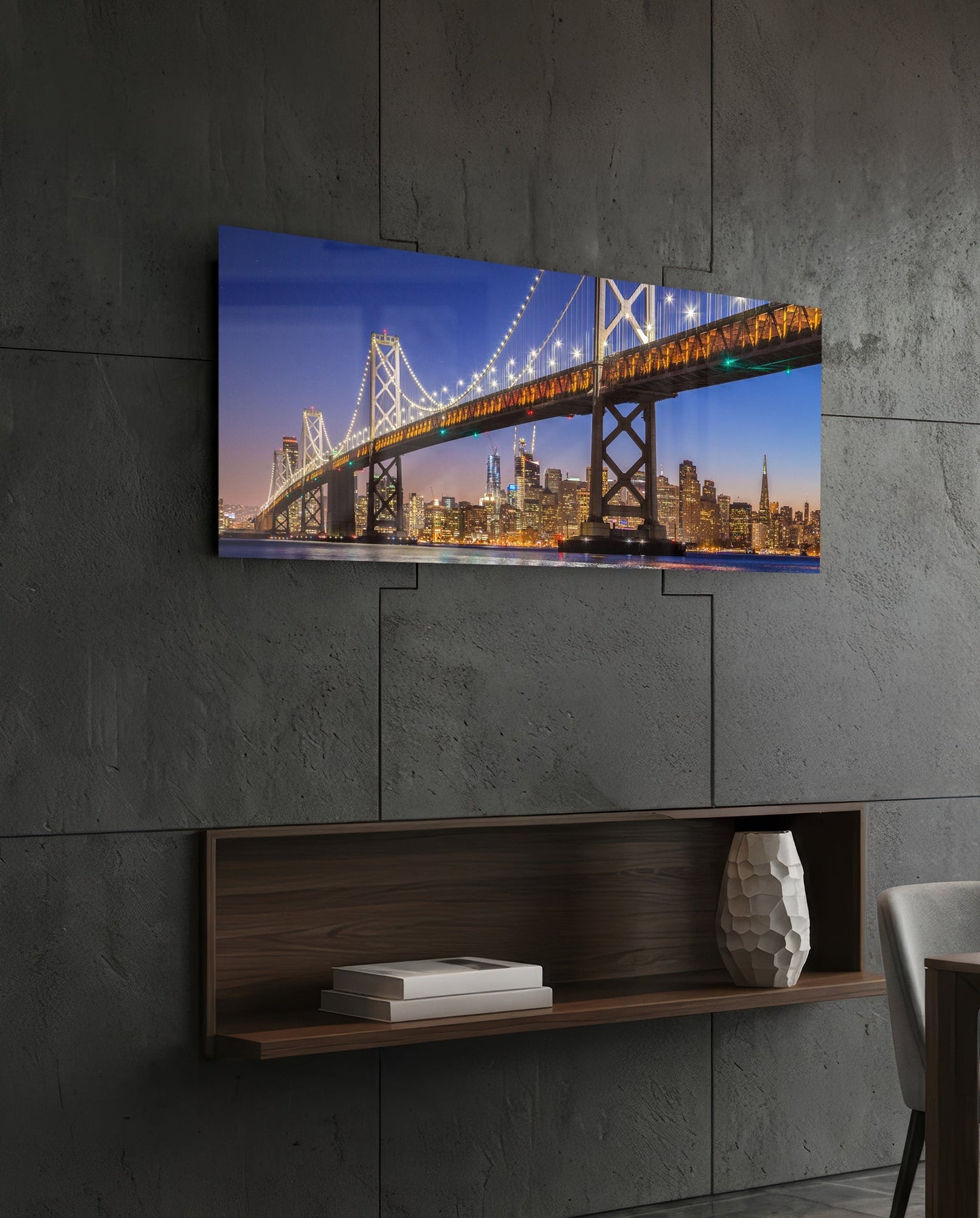 Bay Bridge glass wall art mounted on concrete wall above wooden shelf, showing illuminated bridge and San Francisco skyline at dusk.