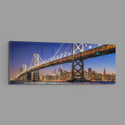Illuminated Bay Bridge spanning San Francisco skyline at twilight, mounted as horizontal glass wall art on gray background.