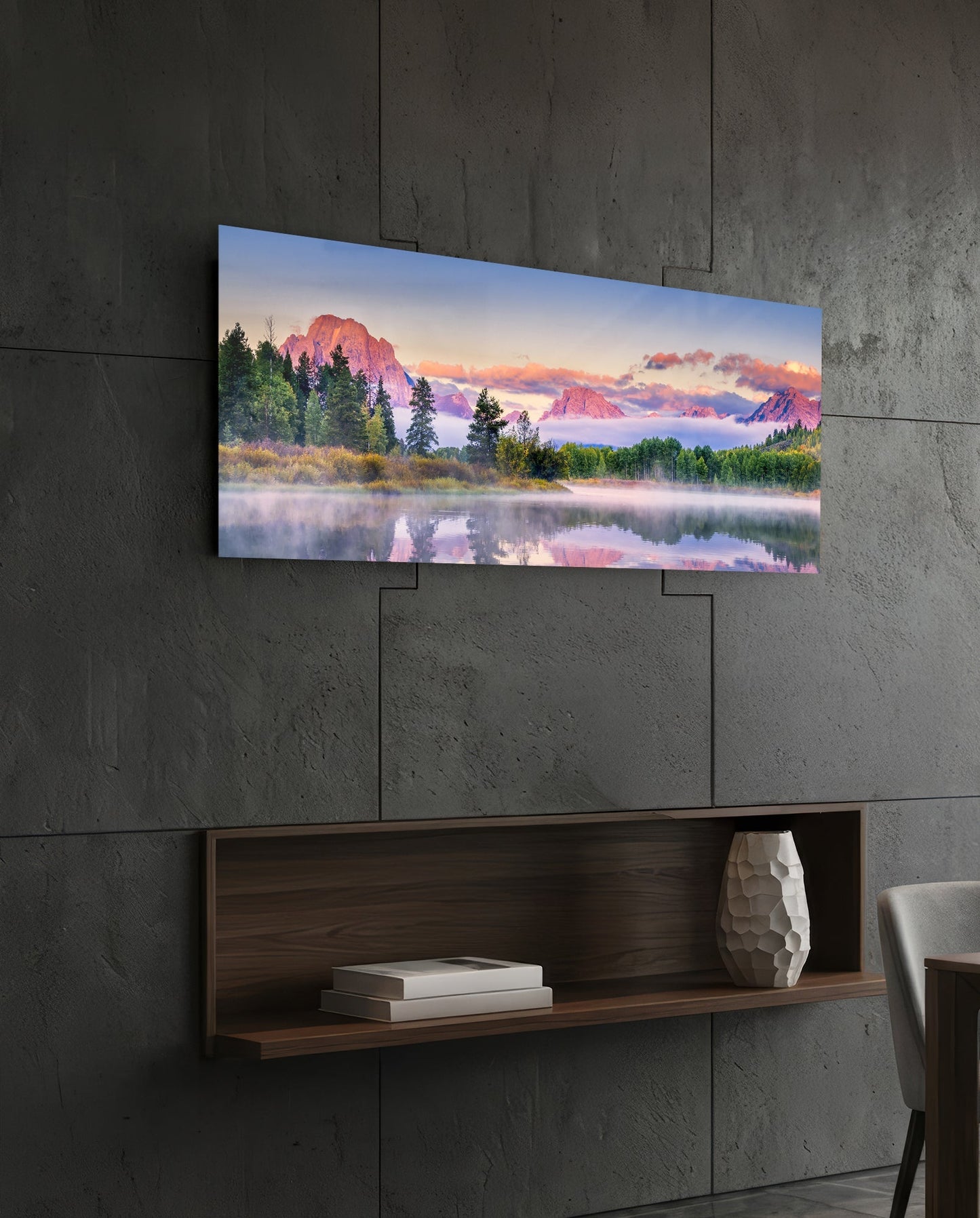 Panoramic glass wall art displaying a misty mountain landscape with pink-hued peaks and forested shoreline, mounted above a wooden shelf on concrete wall.