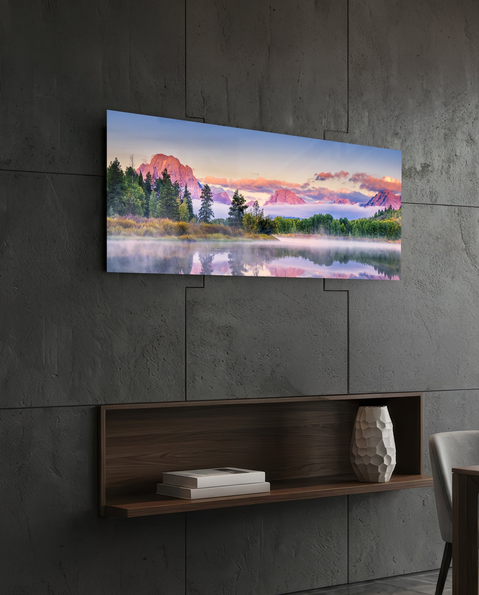 Panoramic glass wall art displaying a misty mountain landscape with pink-hued peaks and forested shoreline, mounted above a wooden shelf on concrete wall.
