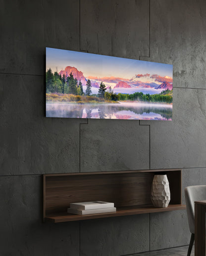Panoramic glass wall art displaying a misty mountain landscape with pink-hued peaks and forested shoreline, mounted above a wooden shelf on concrete wall.