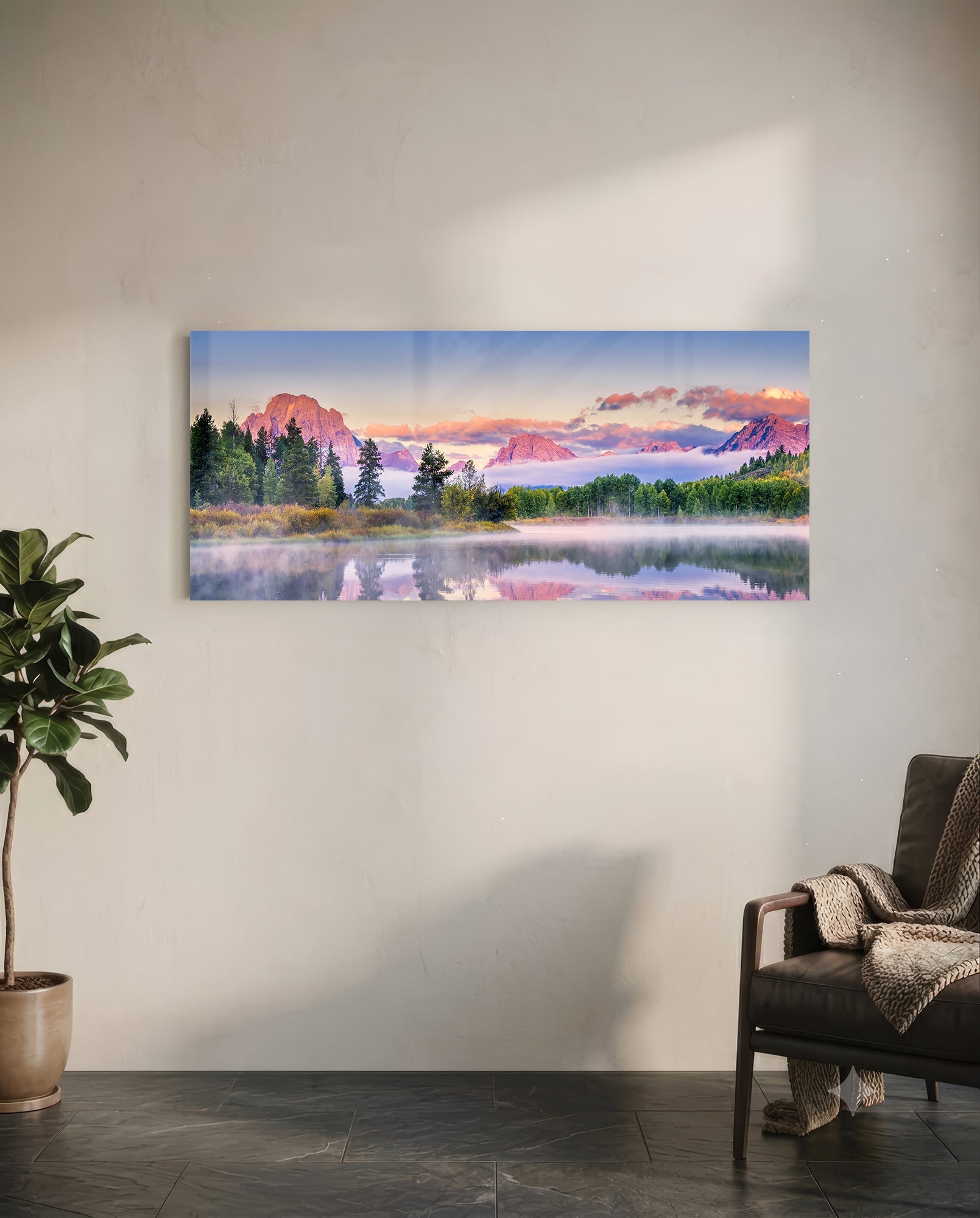 Panoramic glass wall art mounted on white wall showing misty mountain lake landscape with pink sunrise reflection, flanked by potted plant and leather chair.