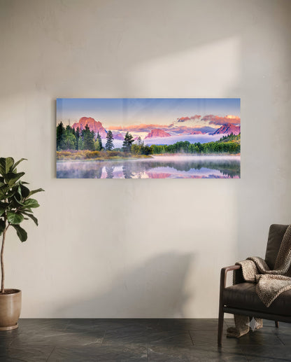 Panoramic glass wall art mounted on white wall showing misty mountain lake landscape with pink sunrise reflection, flanked by potted plant and leather chair.