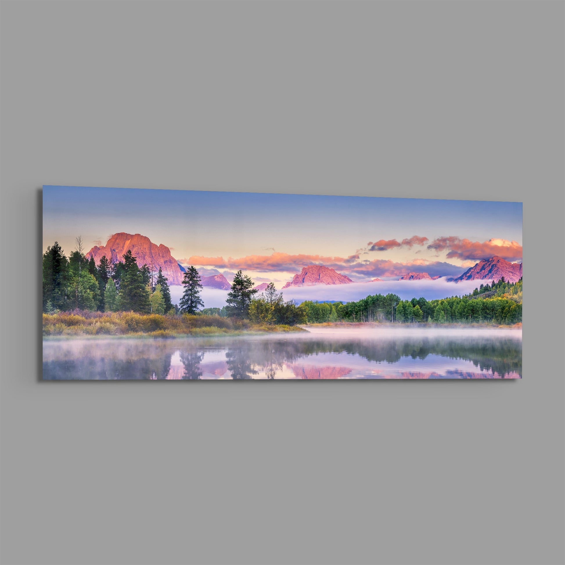 Horizontal glass wall art showing a misty lake at sunrise with forested shoreline and pink-tinted mountains reflected in still water.