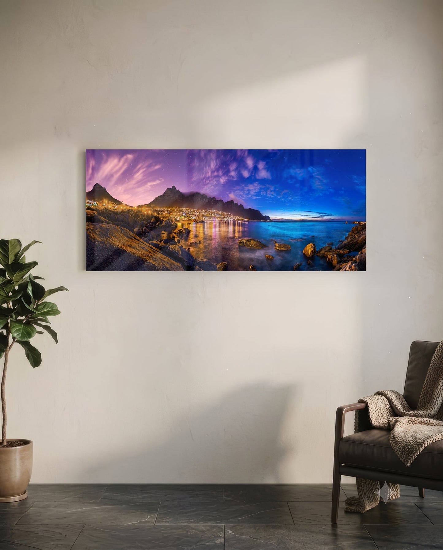 Glass wall art mounted on white wall showing twilight coastal city with illuminated mountains reflected in blue water.